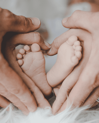 A baby 's feet are being held in the hands of two adults.