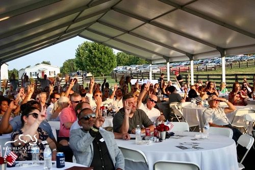 A group of people sitting at tables under a tent.