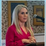 A woman in red shirt speaking at podium.