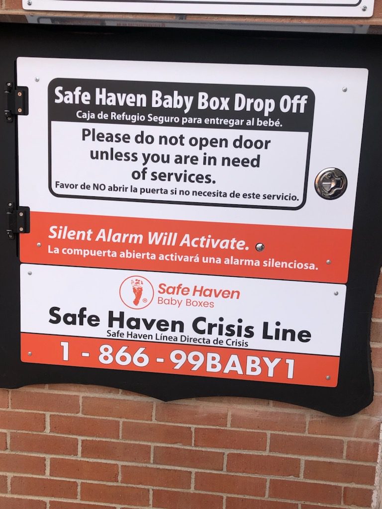 A sign that says safe baby box drop on a brick wall.